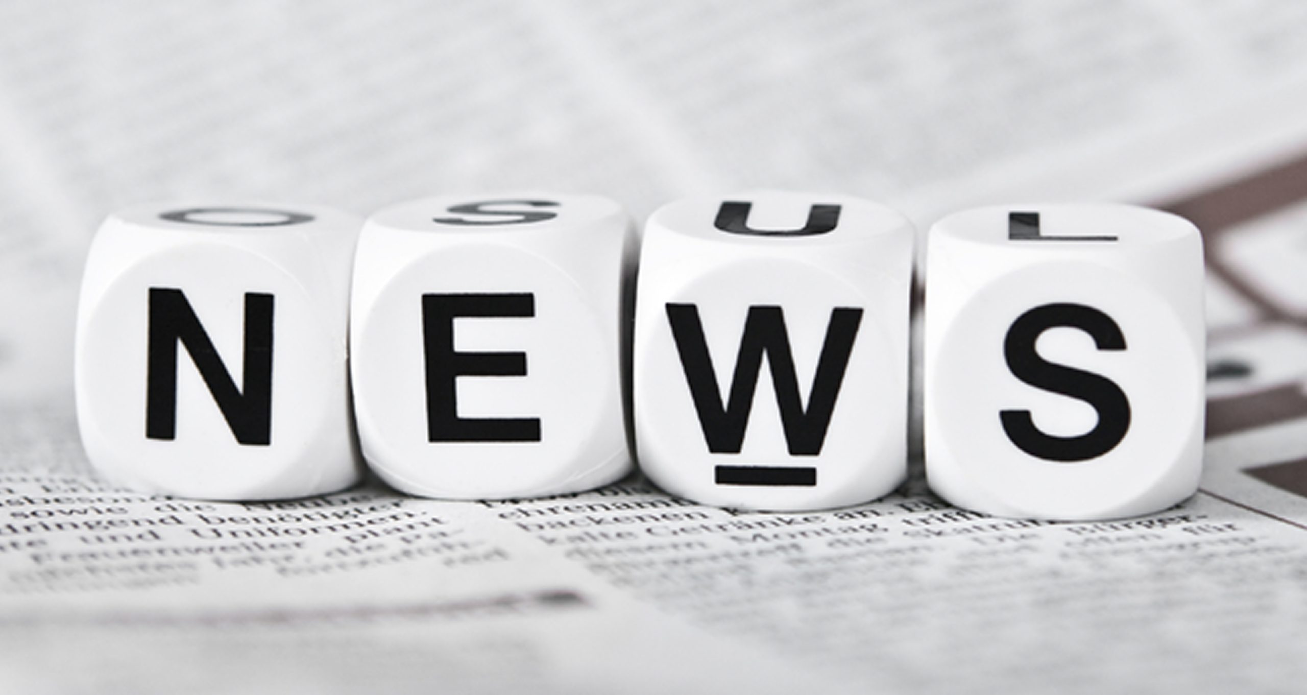 Mot "news" écrit avec des dés (1 lettre par dé). Tout cela posé sur un journal